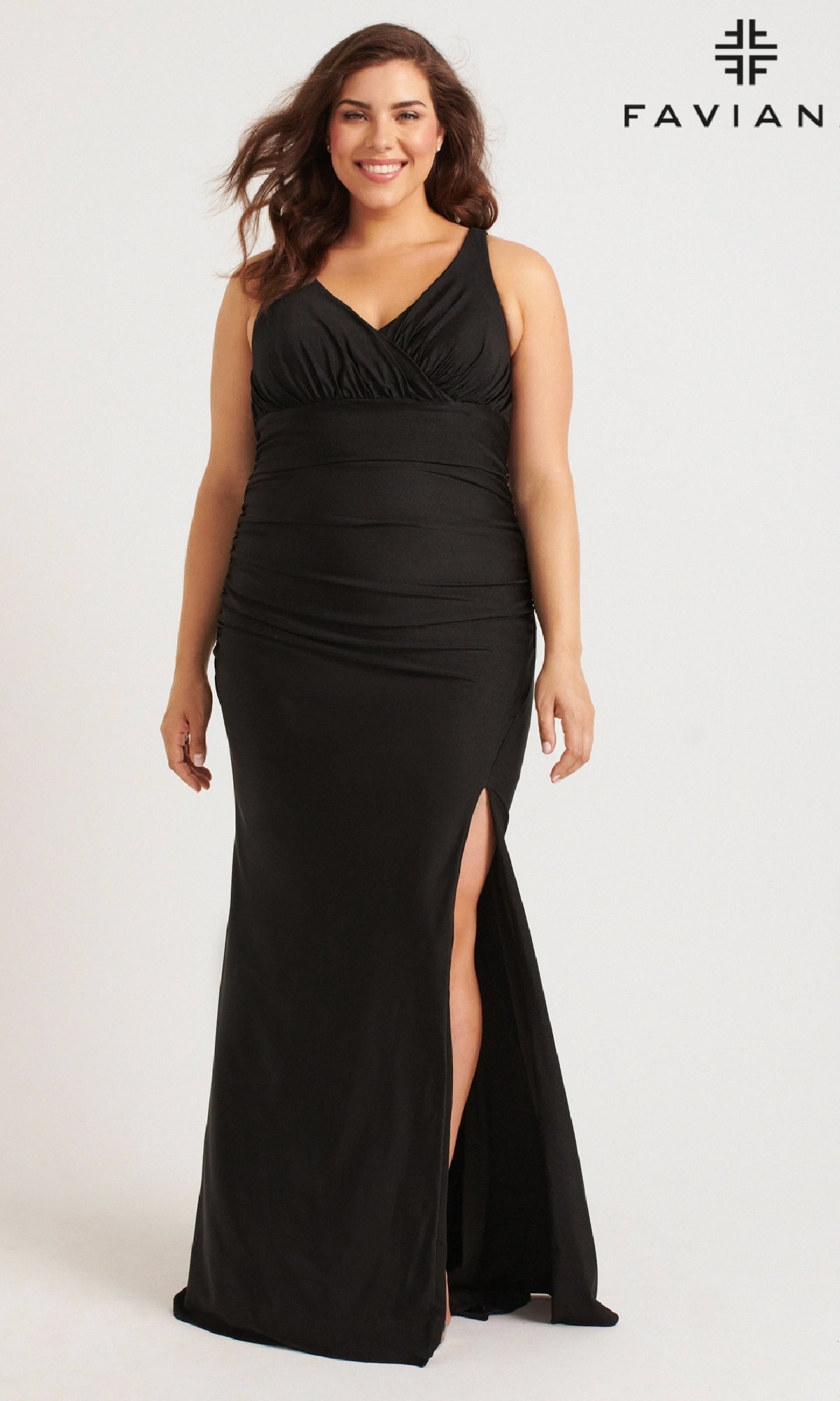 A woman wearing the Faviana 9584 long plus-size black v-neck prom dress with a sleeveless design and side slit stands and smiles in front of a plain background with the Faviana logo.